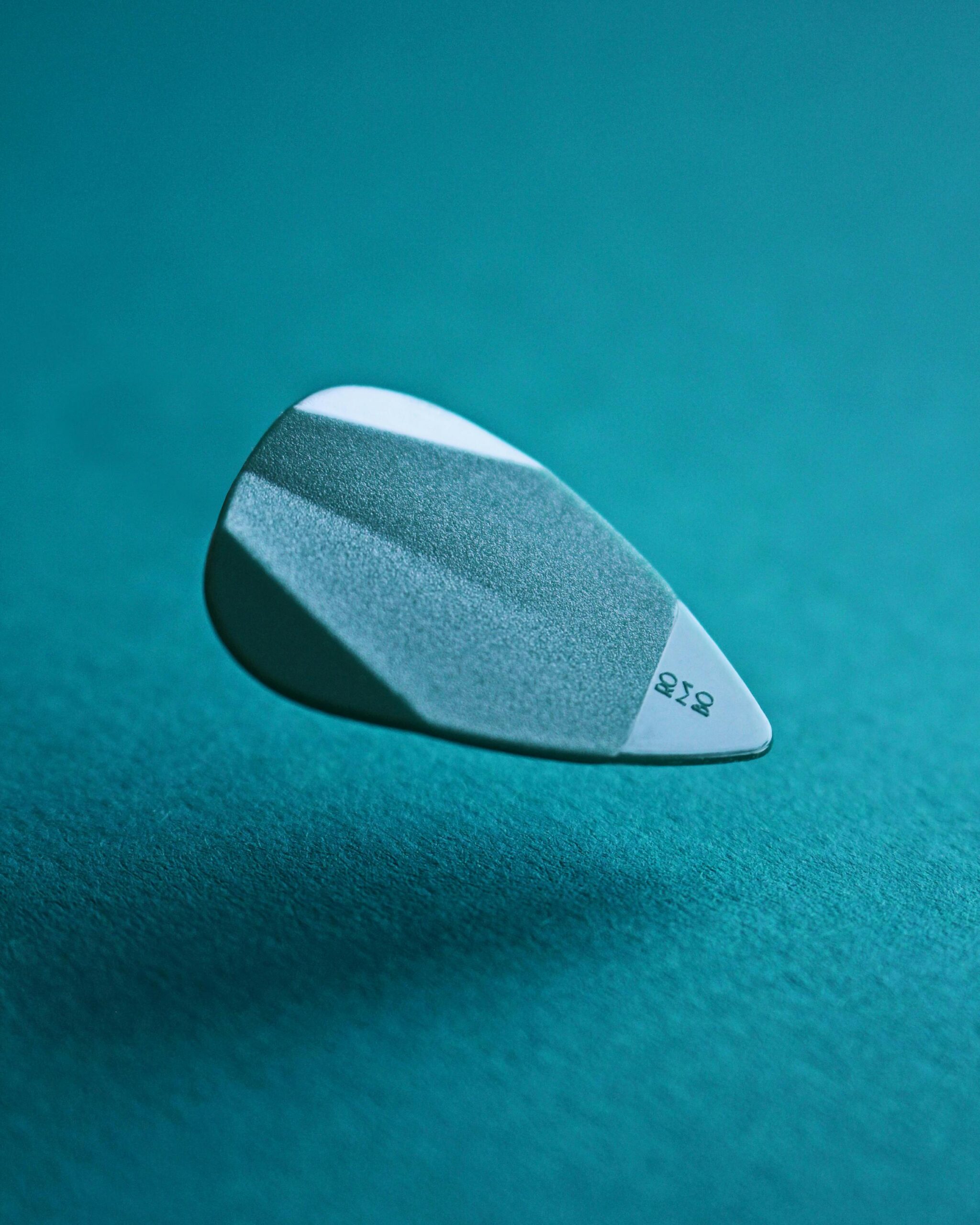 A detailed close-up of a levitating guitar pick against a teal background, showcasing texture.